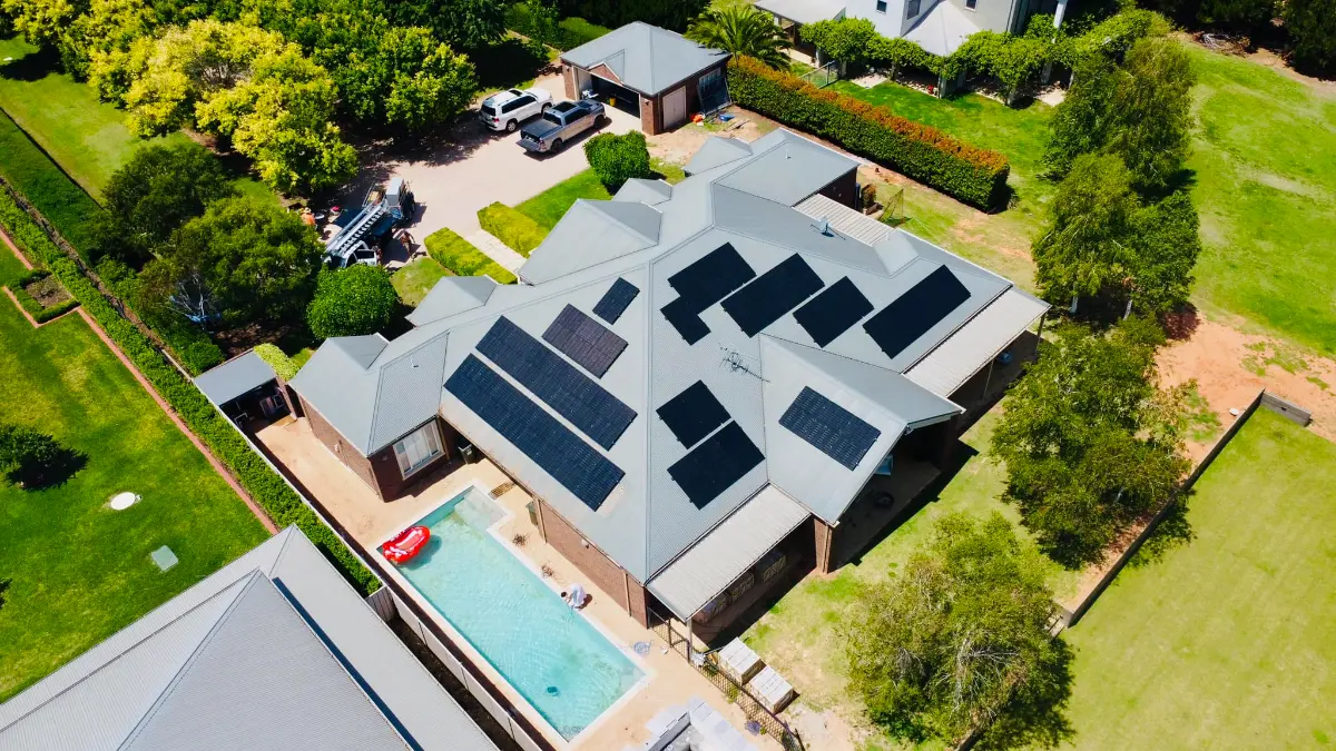 Drone view of a large home with solar panels on several faces of its metal roof, installed by CES