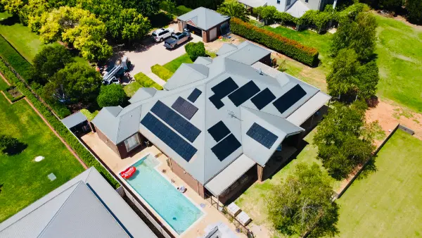 Drone view of a large home with a pool and solar panels on several faces of its grey metal roof