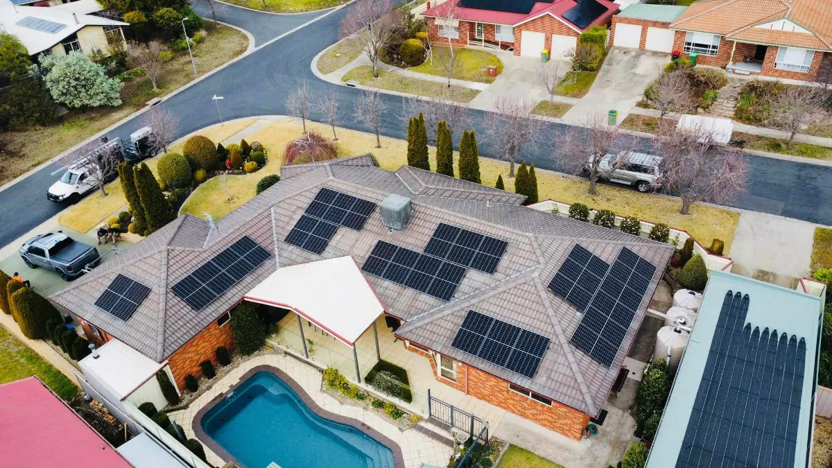 Drone view of a brick home with a swimming pool and solar panels on several sections of its tile roof