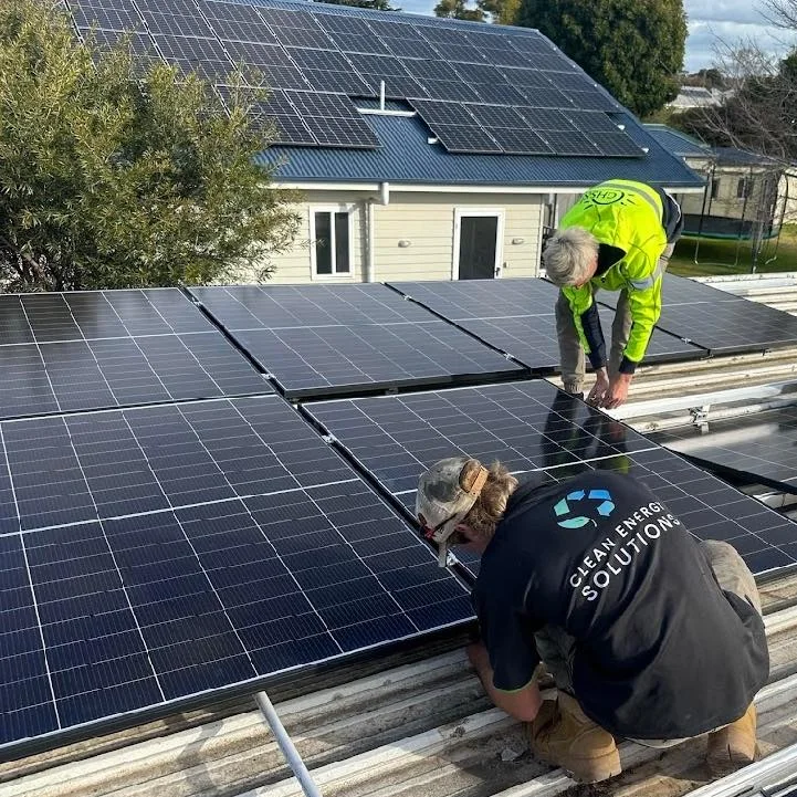 Two CES installers fixing solar panels to rails on a corrugated roof