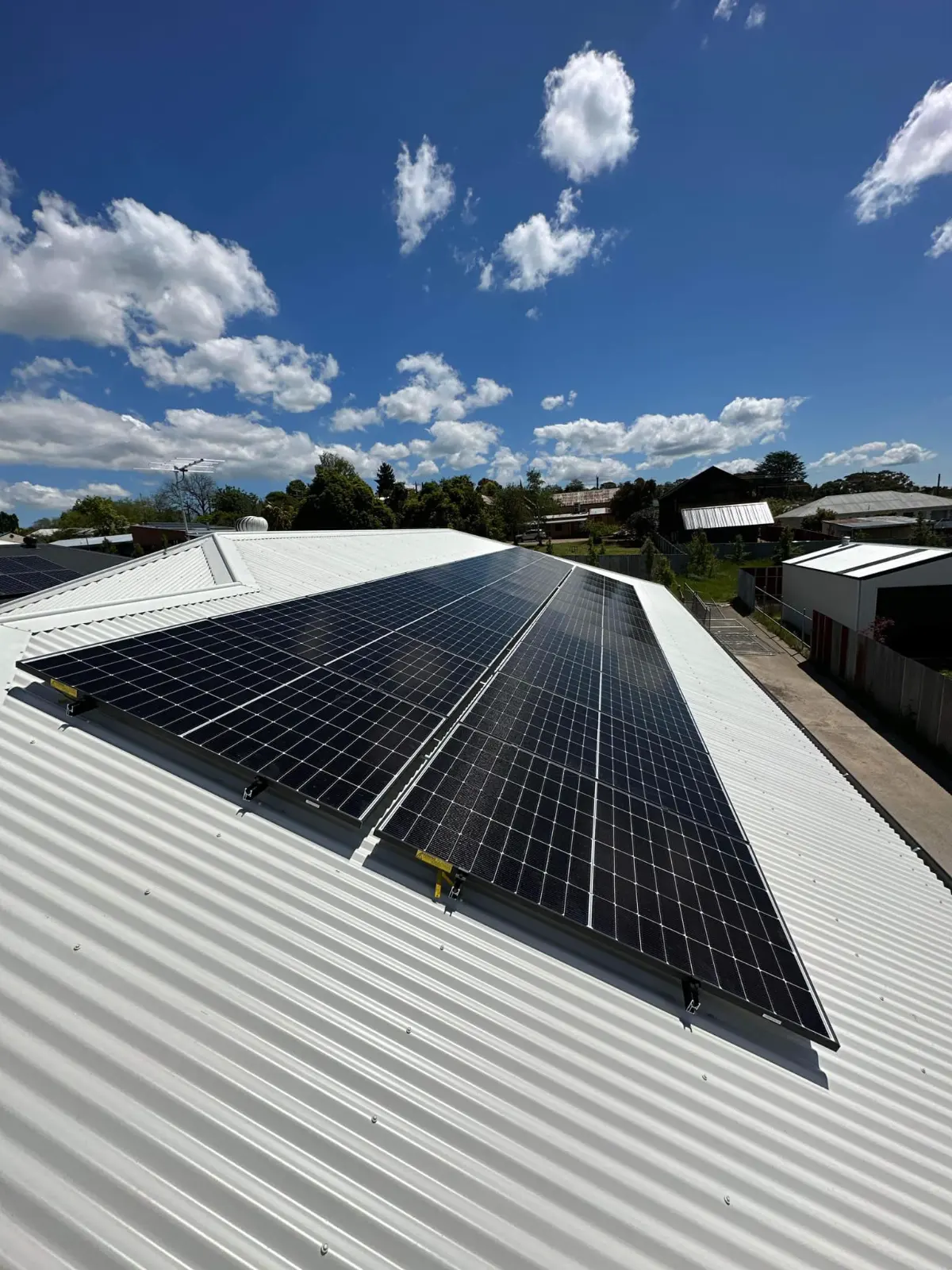 Two rows of solar panels on a white corrugated roof under a bright blue sky, installed by CES