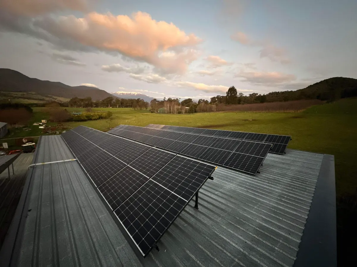 Rows of solar panels on a farm shed roof at sunset with paddocks behind, installed by CES