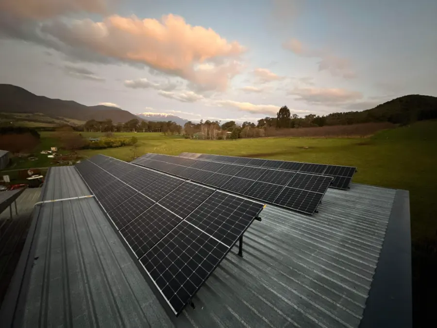 Rows of solar panels on a farm shed roof at sunset with paddocks behind, installed by CES
