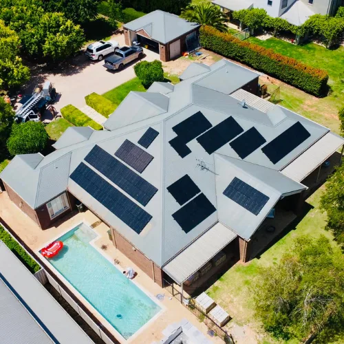 Drone view of a home with a hipped Colorbond roof, a swimming pool and solar panels on several roof faces