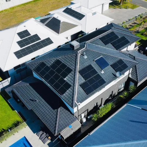 Drone view of a two-storey home with a dark tile roof and solar panels on several roof sections