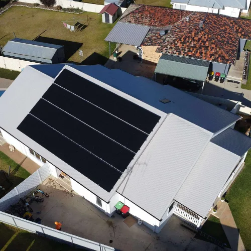 Drone view of a home with a light tin roof and a single large block of black solar panels on one side