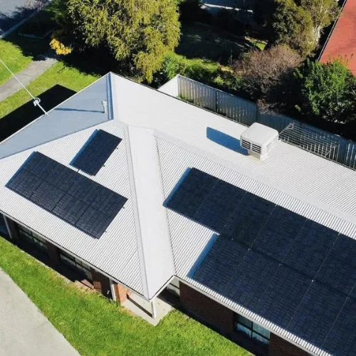 Drone view of a home with a pale tin roof and black solar panels on three roof faces