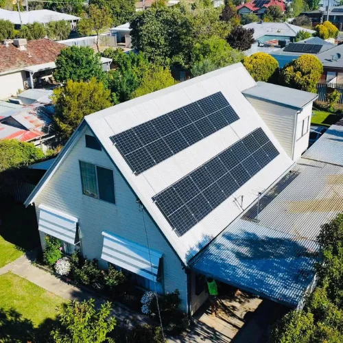 Drone view of a weatherboard house with two rows of solar panels on its steep tin roof
